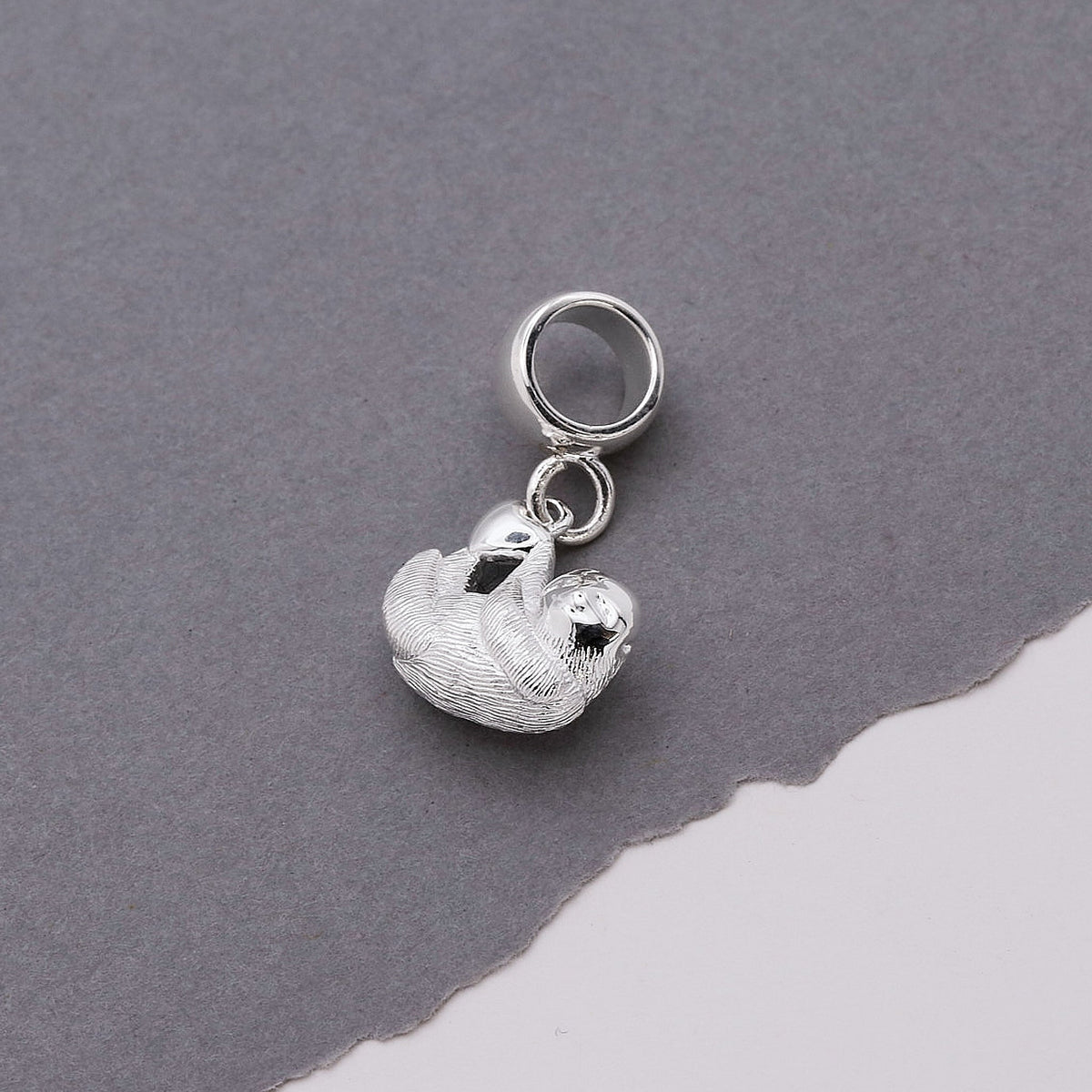 A silver sloth charm shaped like a small hanging pendant by Scarlett Jewellery.