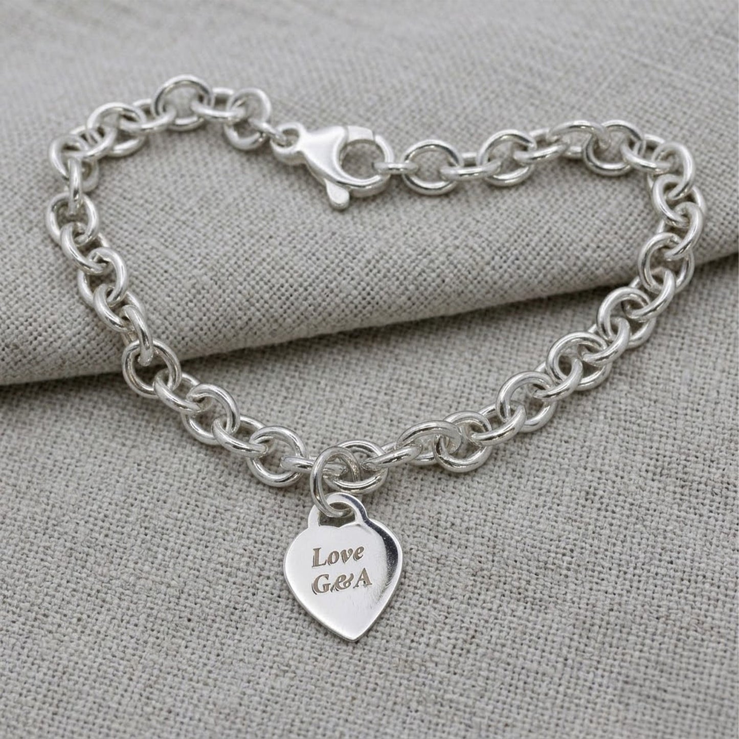 A silver heart tag charm bracelet with personalized engraving, featuring a delicate chain and small heart-shaped pendant by S