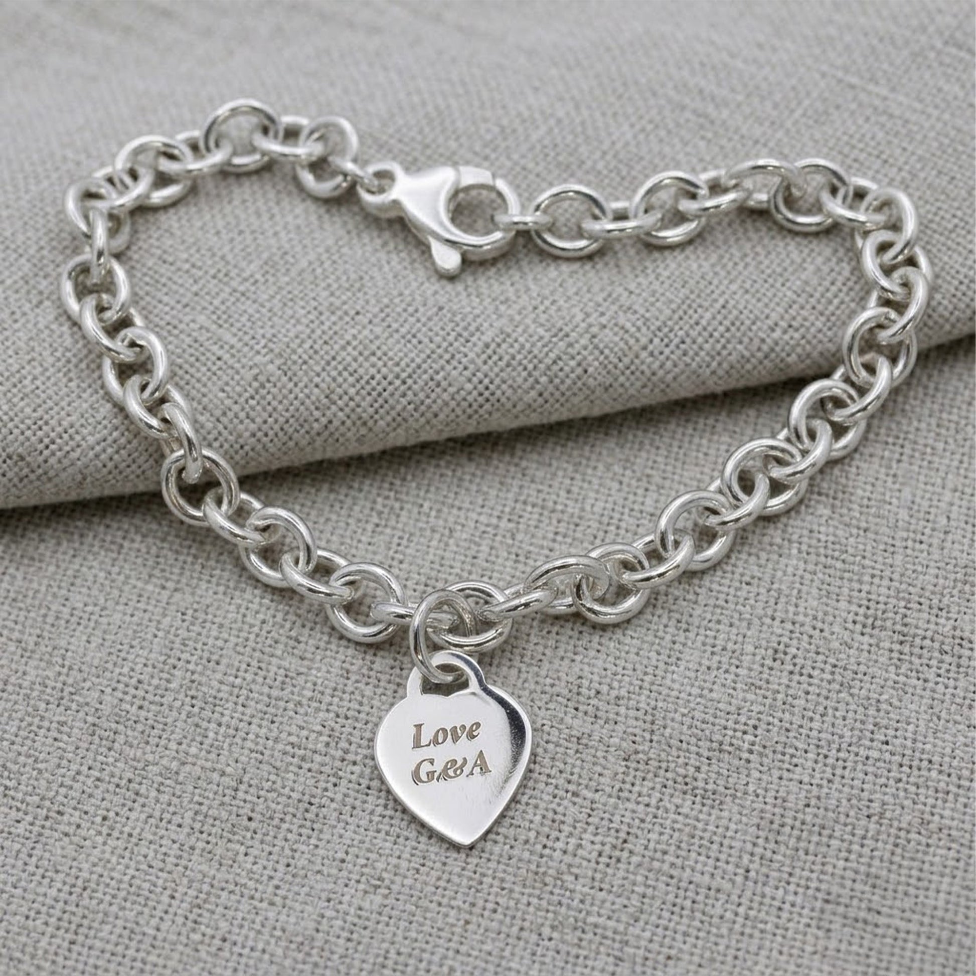 A silver heart tag charm bracelet with personalized engraving, featuring a delicate chain and small heart-shaped pendant by S