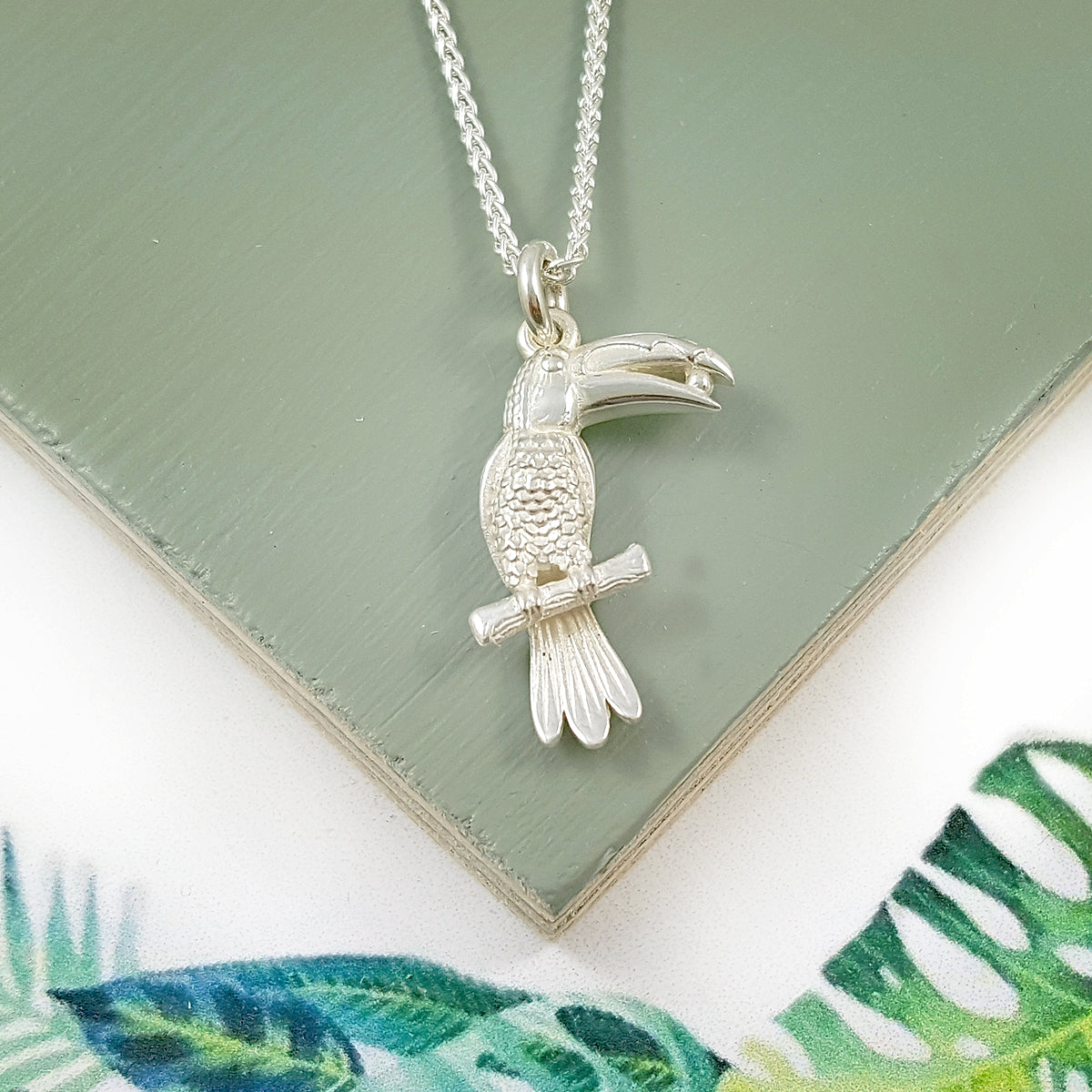 A silver toucan parrot charm with detailed feather texture, displayed on a white background by Scarlett Jewellery.
