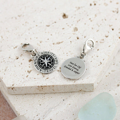 Silver compass charm with personalized engraving, styled on a travel-themed background by Scarlett Jewellery.