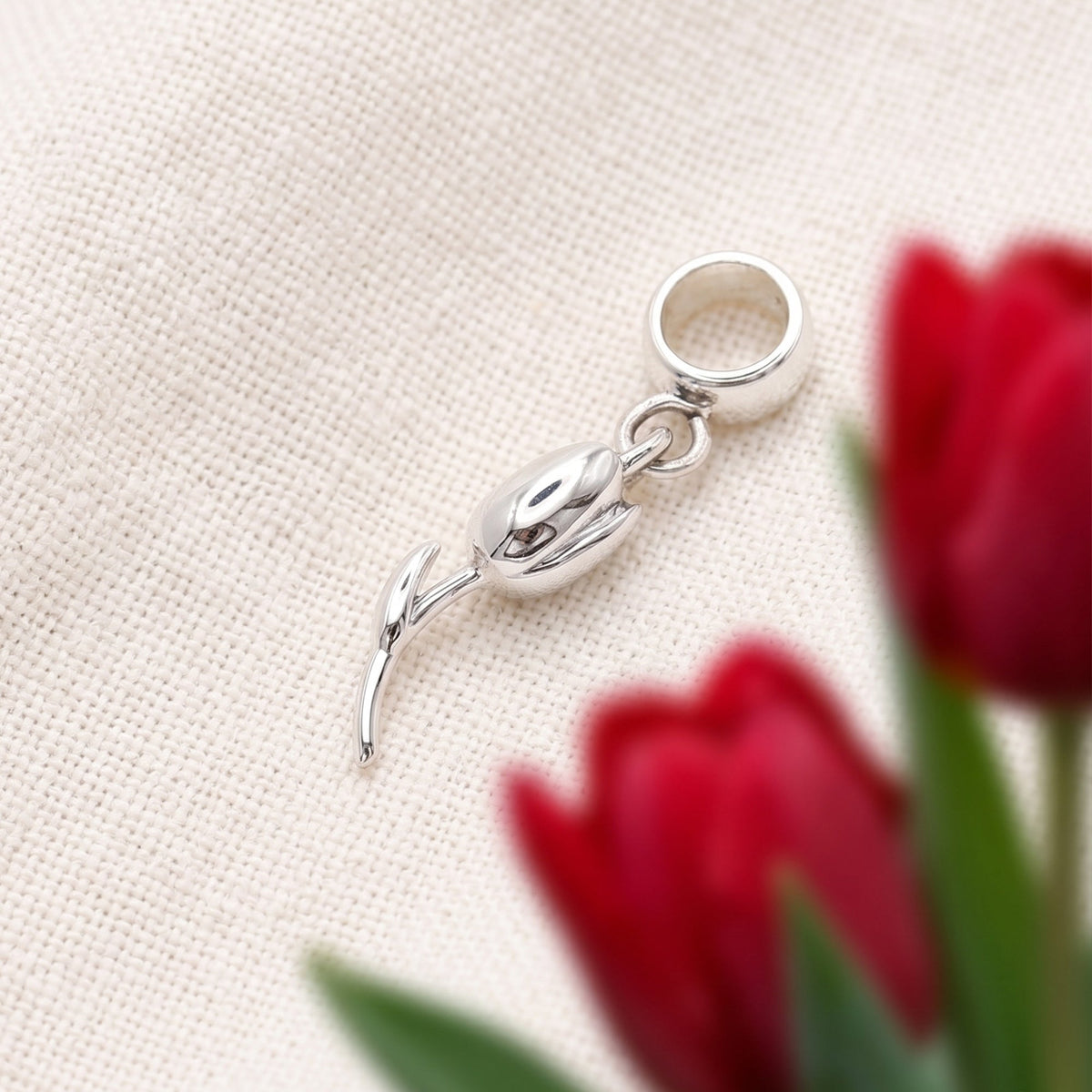 A silver tulip flower charm with intricate detailing, displayed on a soft white background, by Scarlett Jewellery.