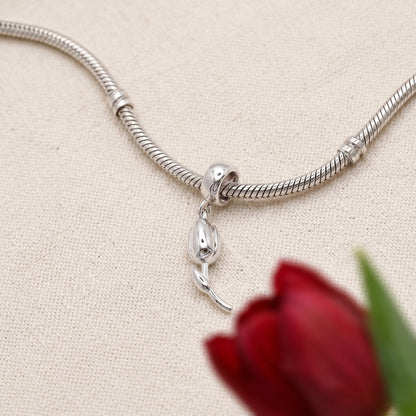 A silver tulip flower charm with intricate detailing, displayed on a soft pink background, by Scarlett Jewellery.
