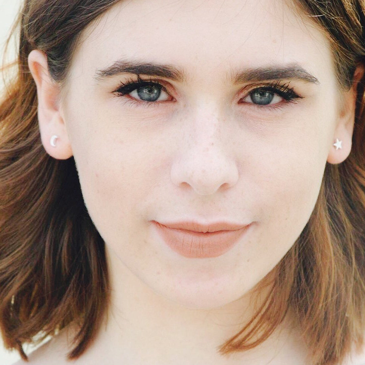 Silver stud earrings with a twinkling star design, styled on a soft background by Scarlett Jewellery.